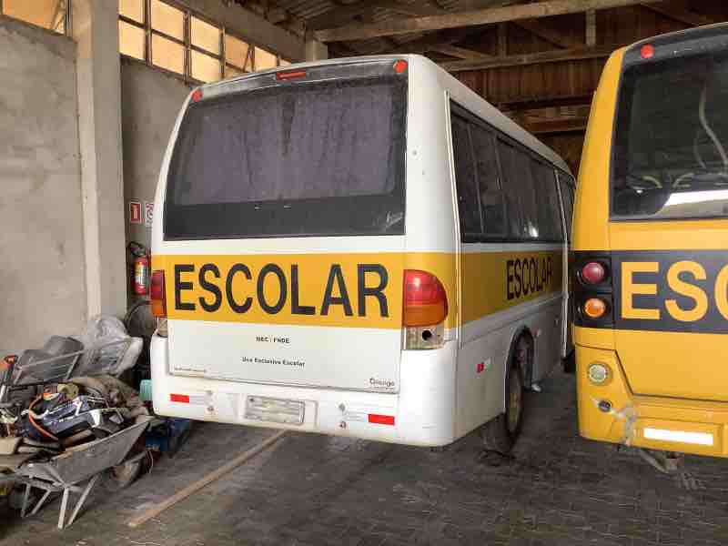 Ônibus escolar estacionado em galpão fechado, com sinais de desuso, como parte do serviço de avaliação de bens inservíveis para o poder público.