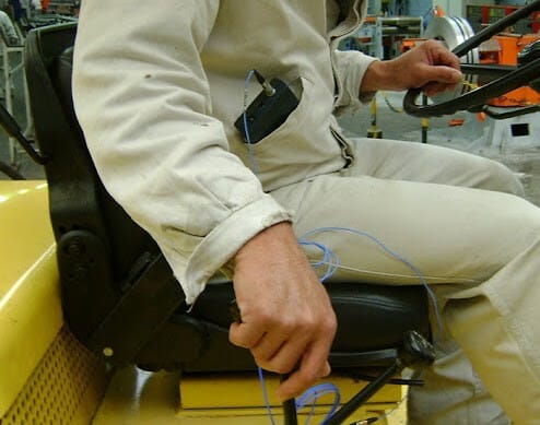 Trabalhador sentado em veículo operacional com sensores conectados ao corpo para medição de vibração ocupacional, representando serviços de engenharia de segurança do trabalho de exposição a vibrações no ambiente de trabalho.
