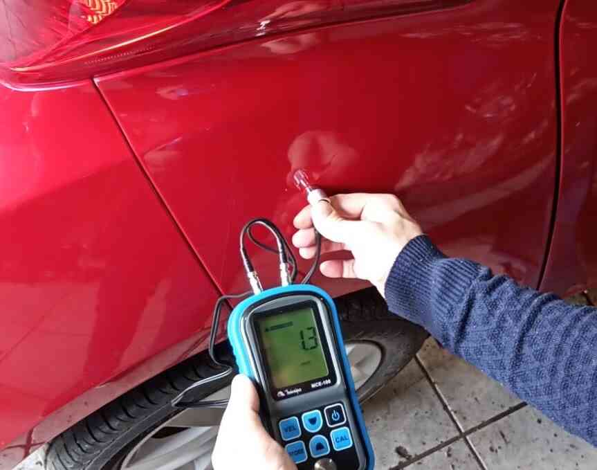 Inspeção técnica em veículo vermelho utilizando equipamento de ultrassom para identificar danos ocultos, representando serviços de perícia em reparos disfarçados sob a pintura.