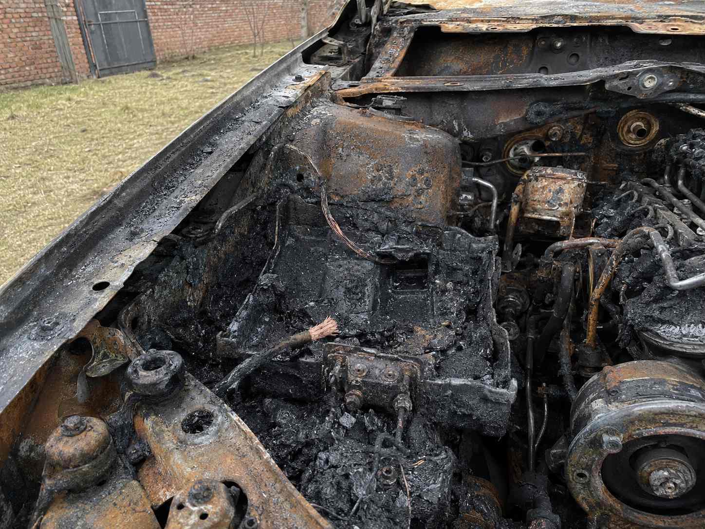 Fotografia forense de motor de carro queimado mostrando resíduos de bateria e cabos elétricos oxidados para análise de hipótese de incêndio elétrico automotivo em São Leopoldo - RS.